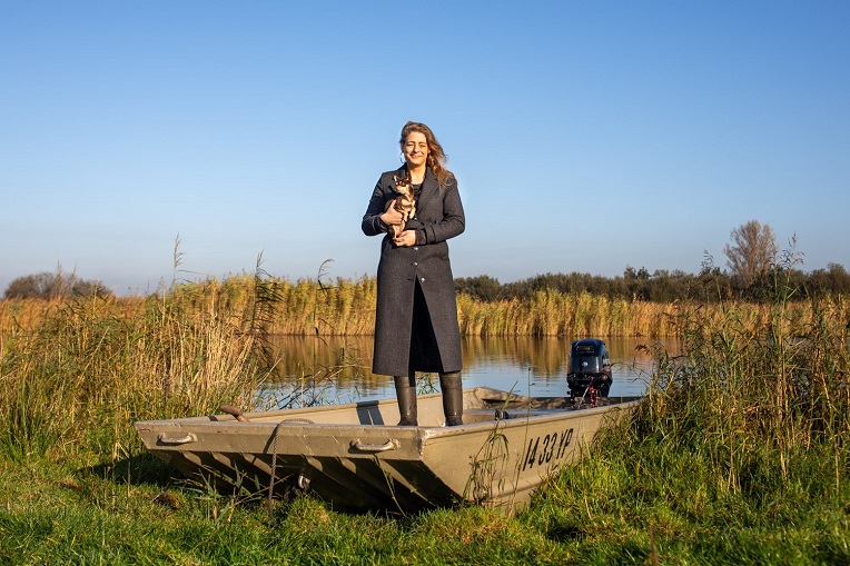 Rosemarijn Dral met hondje op de arm, op een boot in de rietkragen van het Oostzanerveld